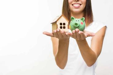 image d'une femme qui tient une maquette de maison dans une main et une tirelire dans l'autre